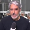 Com camiseta preta informal, William Bonner segura microfone com canopla da Globo no Jornal Nacional de 11 de maio de 2024